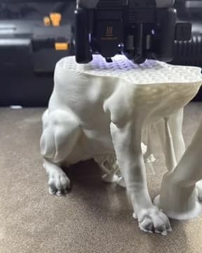 White dog sculpture partway through printing, with the print head on the top layer and supports beside the body.