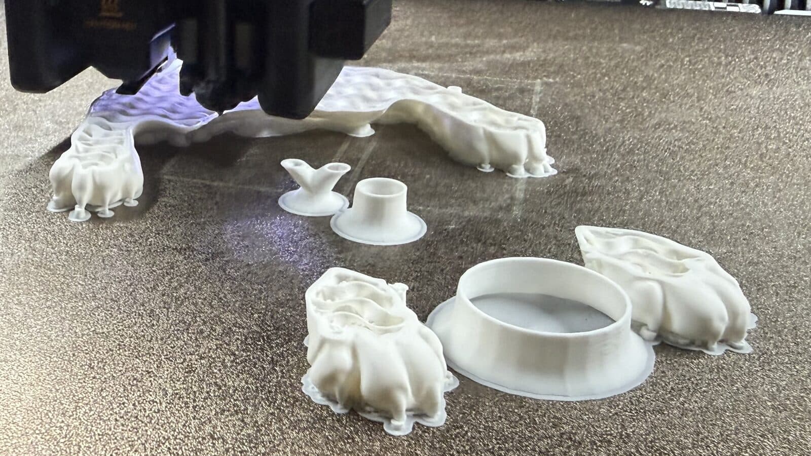 Sculpture parts on a 3D printer bed, showing hollow, thin-walled interiors that use very little plastic.